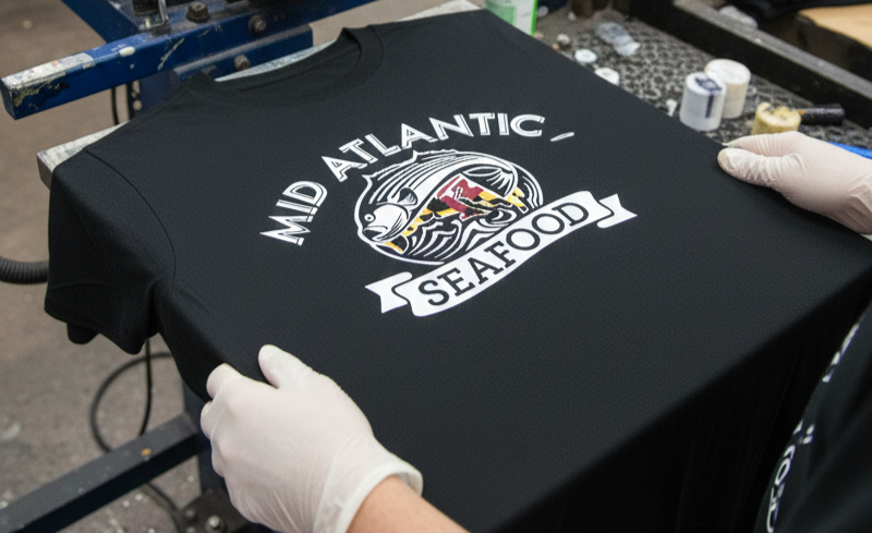 Close-up of screen printed uniforms featuring the Mid Atlantic Seafood logo with Maryland flag design, highlighting puff print restaurant apparel and restaurant uniform printing that turns staff gear into a wearable brand.