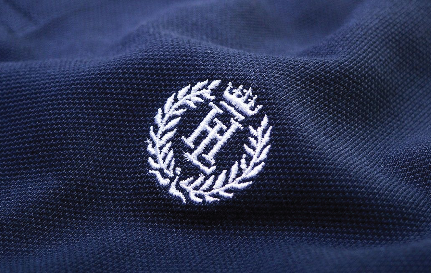 Embroidery vs. Screen Printing comparison—detailed embroidered emblem on textured fabric highlights the premium, dimensional quality of stitched logos.